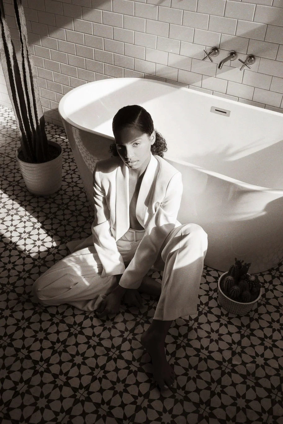 Girl wearing a white suit sitting on tiled floor beside a bathtub